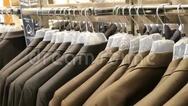 棕色和灰色的<strong>男士</strong>`夹克挂在商场的<strong>男士</strong>服装店的衣架上。 一大群男人穿`西装